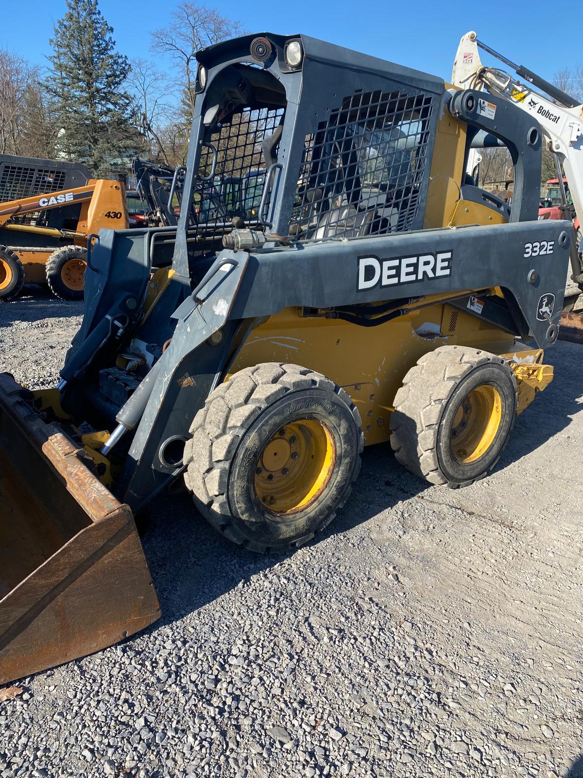 A John Deere 332E skid steer loader and other machines staged in a contractor's yard.